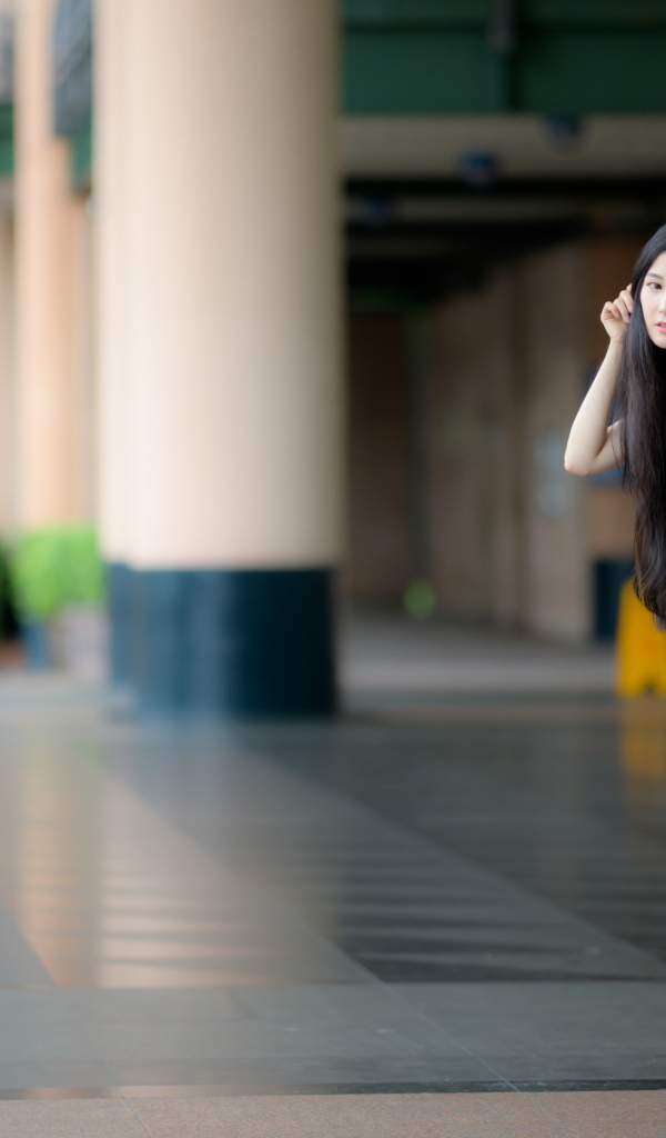 Стройная азиатка в коротком платье  стоит у колонны