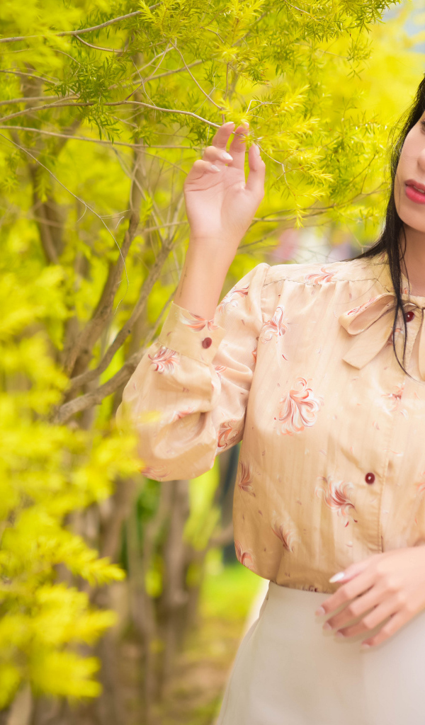 Молодая девушка азиатка стоит у дерева с зелеными листьями