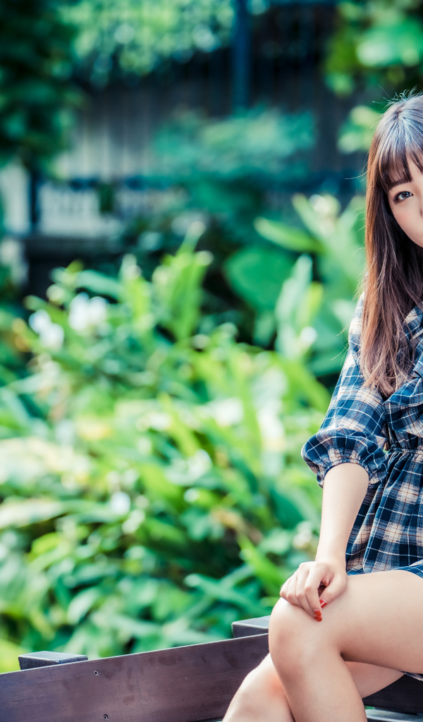 Молодая девушка в клетчатом платье сидит на заборе