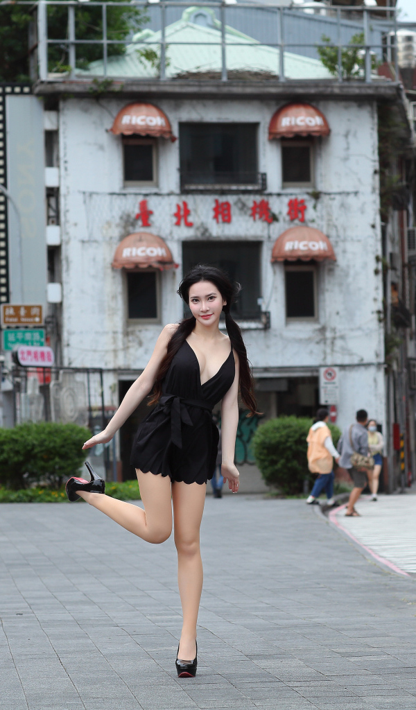 Девушка азиатка в черном платье стоит у дома