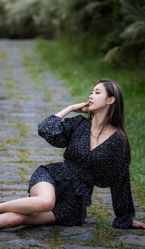 Девушка азиатка в платье лежит на дороге в парке