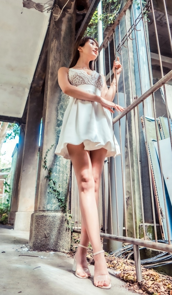 Девушка азиатка в платье стоит у решетки 