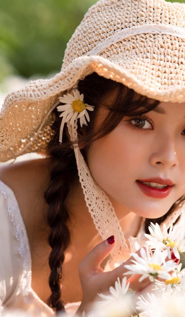 Девушка азиатка в шляпке на поле с ромашками