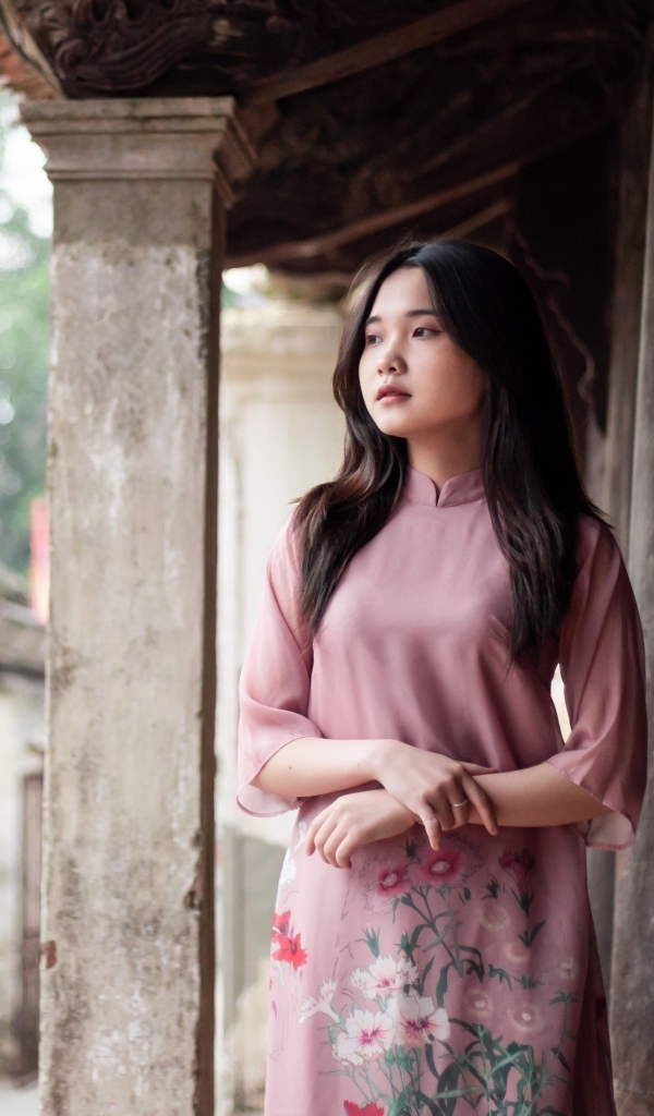 Девушка азиатка в розовом платье стоит у дома