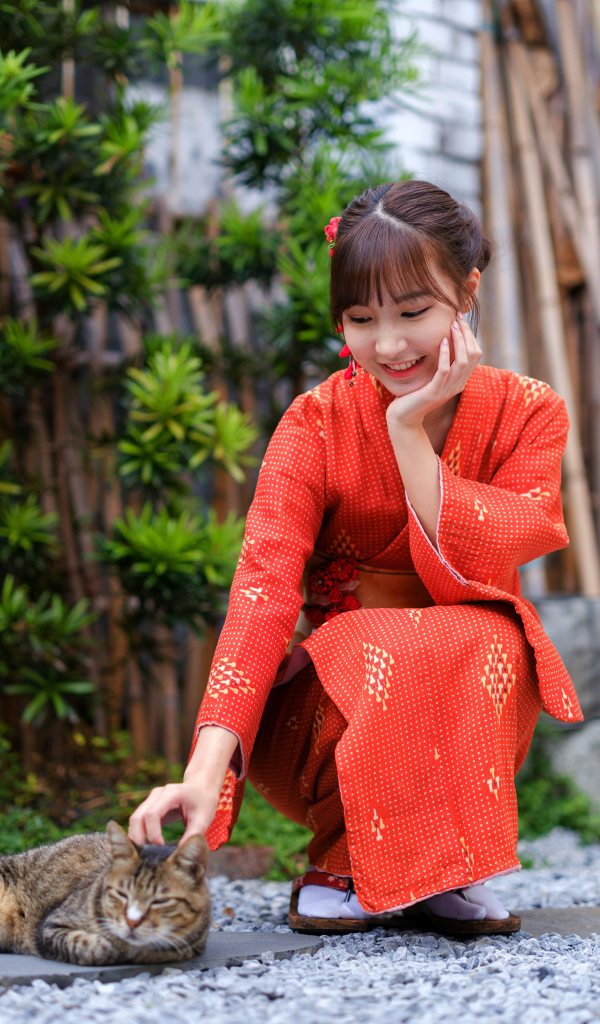Девушка азиатка в красном платье гладит кота