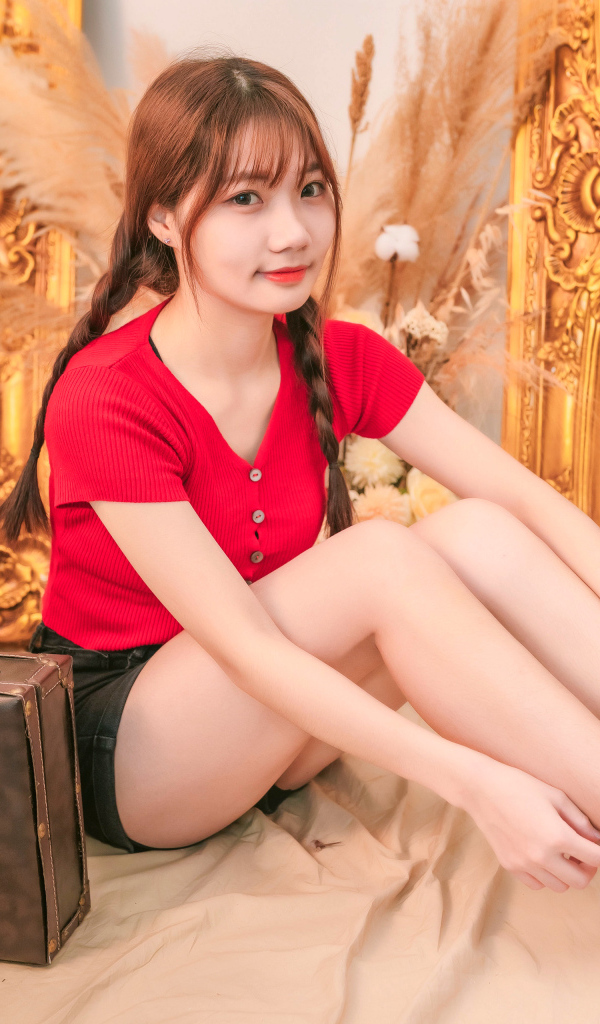 Девушка азиатка сидит на полу с чемоданом