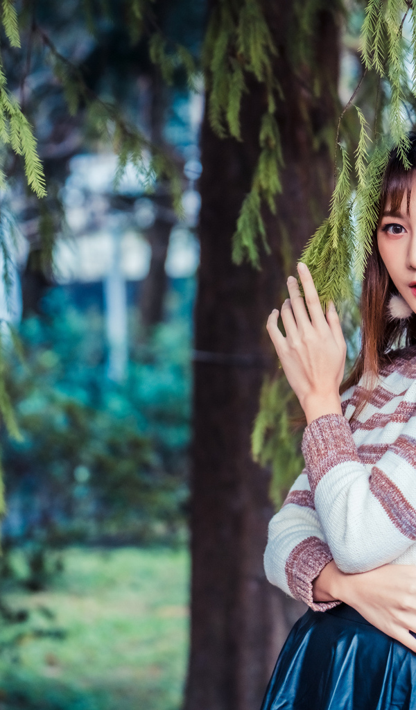 Девушка азиатка стоит у дерева ели