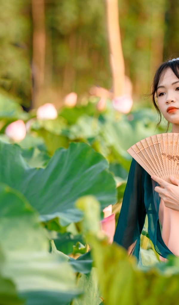 Девушка азиатка с веером в зеленых листьях лотоса