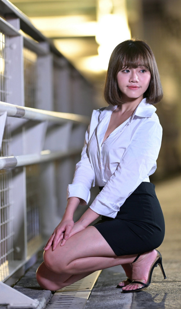 Азиатка в белой блузке и черной юбке сидит на корточках