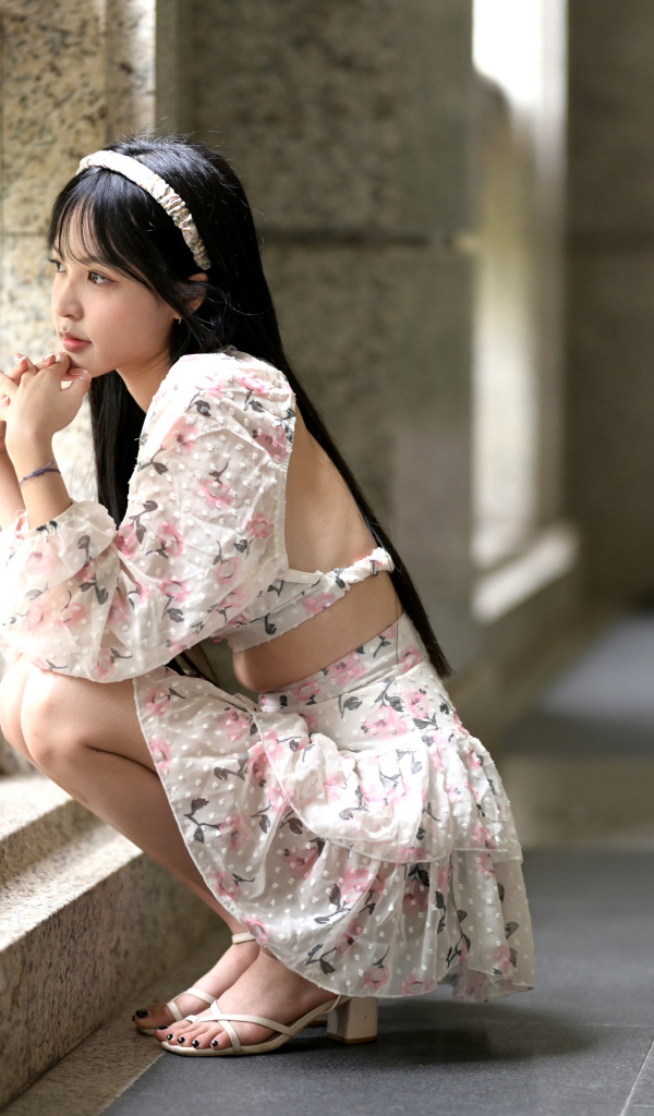 Красивая девушка азиатка в костюме сидит у стены