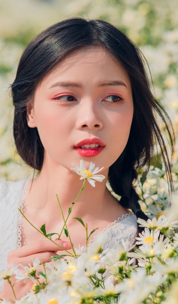 Красивая девушка азиатка на поле с белыми ромашками