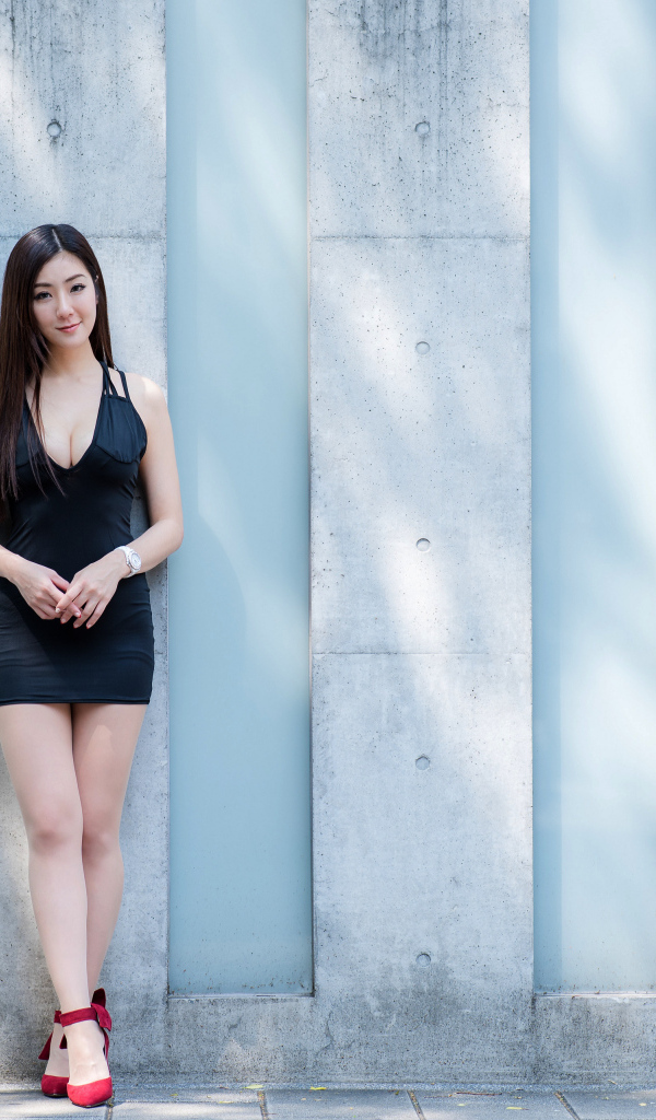 Красивая азиатка в коротком платье стоит у стены