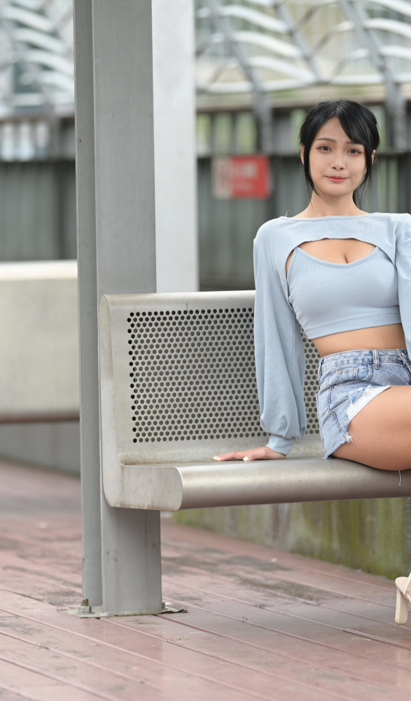 Красивая темноволосая девушка азиатка сидит на лавке