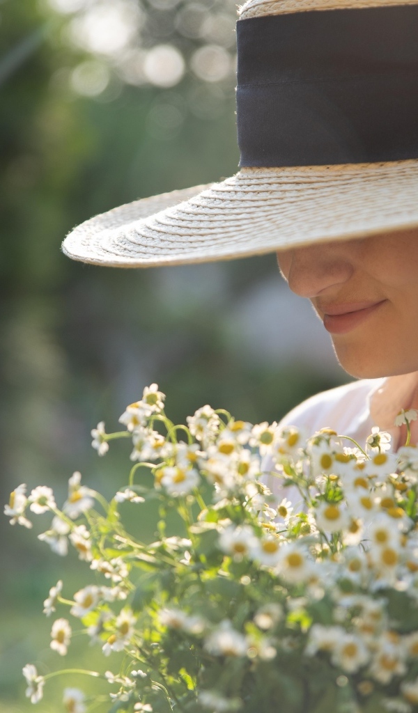 Красивая девушка в шляпе с букетом ромашек