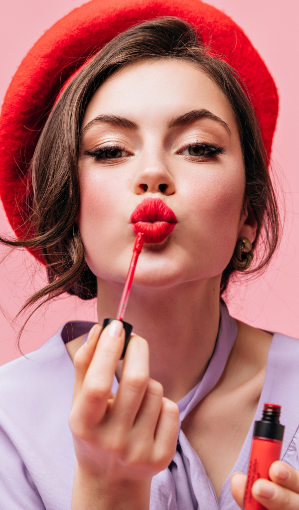 Красивая девушка в красном берете красит губы