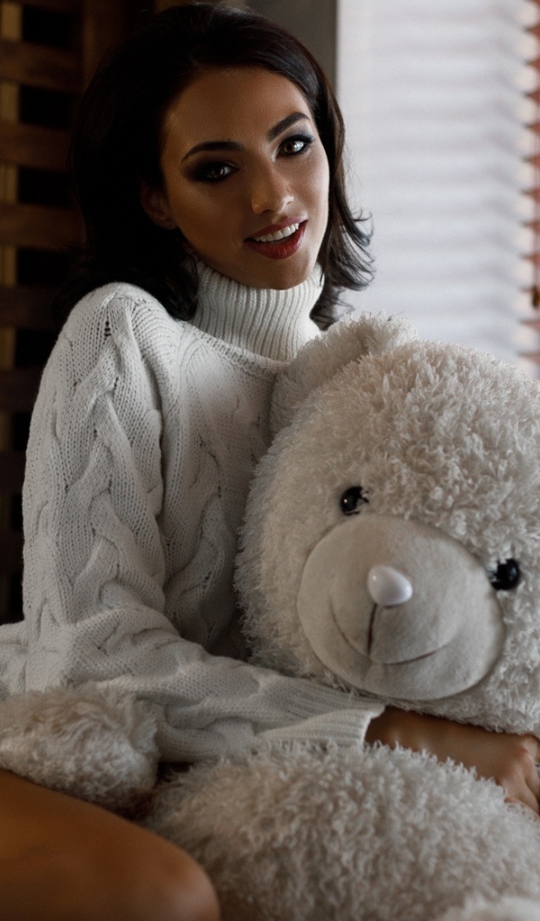 Красивая девушка в свитере с медведем у окна