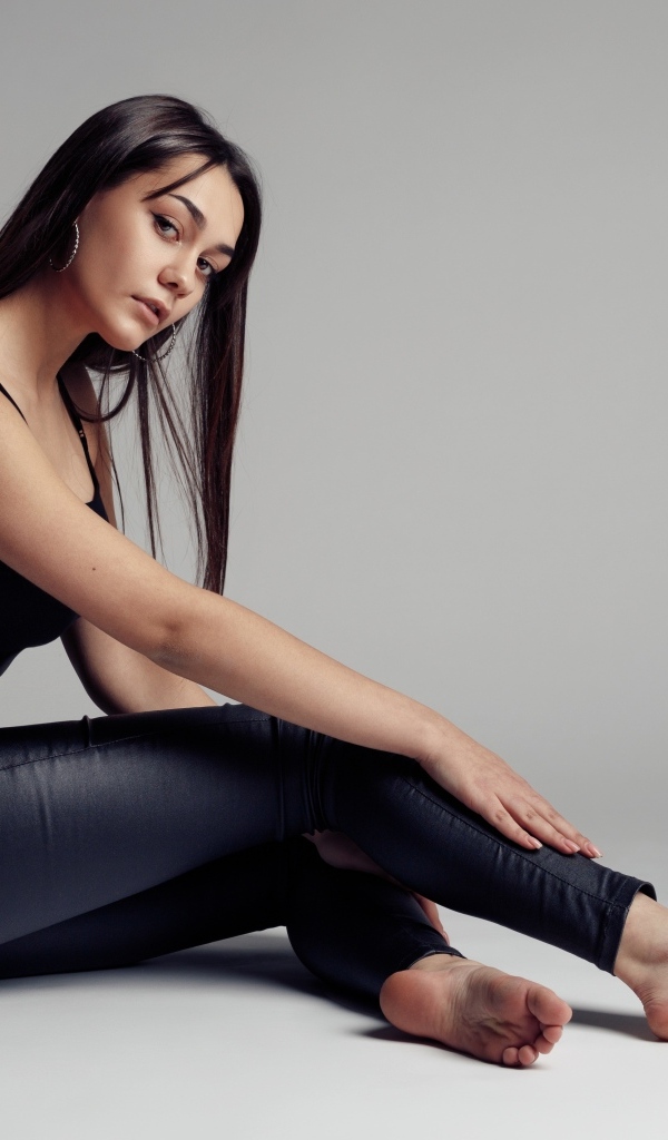 Красивая девушка в черных брюках на сером фоне