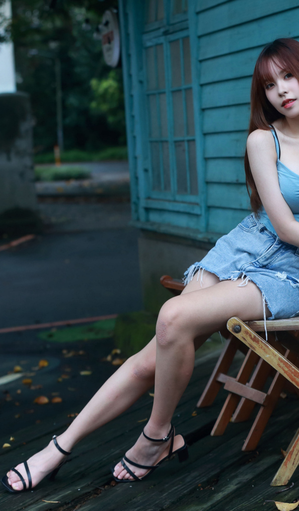 Красивая девушка сидит на стуле у дома