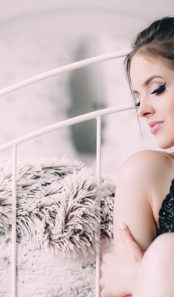 Красивая девушка сидит на полу у кровати 