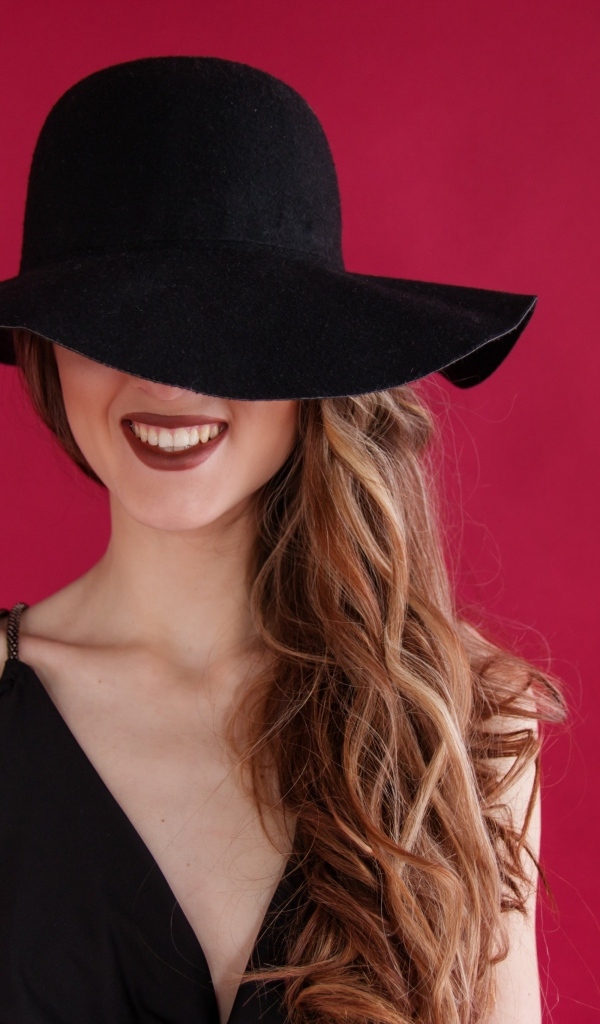 Черная шляпа на лице у девушки на розовом фоне