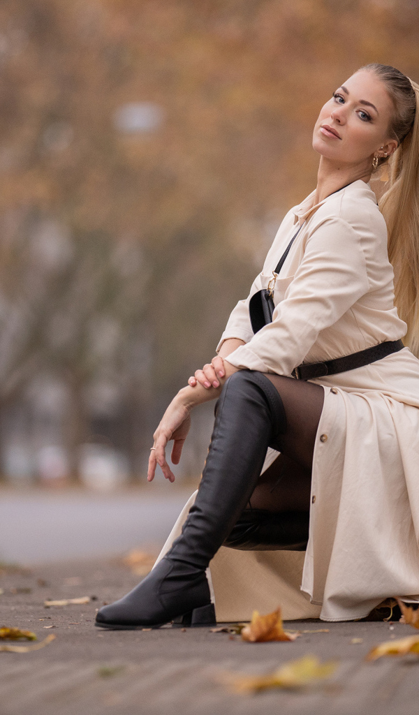 Девушка блондинка сидит в пальто в парке
