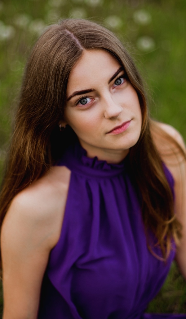 Милая девушка в фиолетовом платье сидит на траве