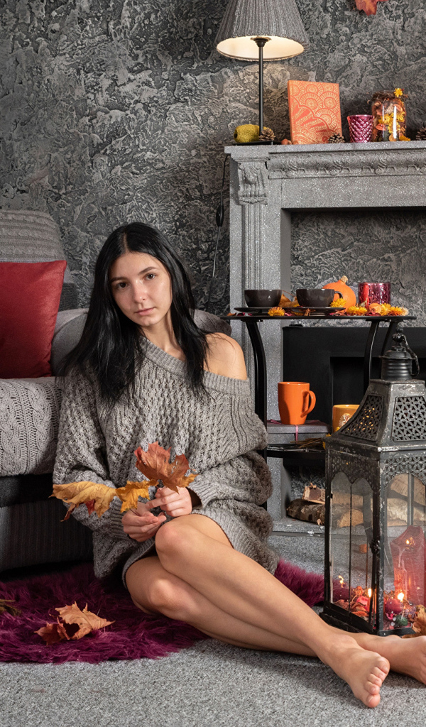 Милая девушка в теплом свитере сидит в комнате с камином