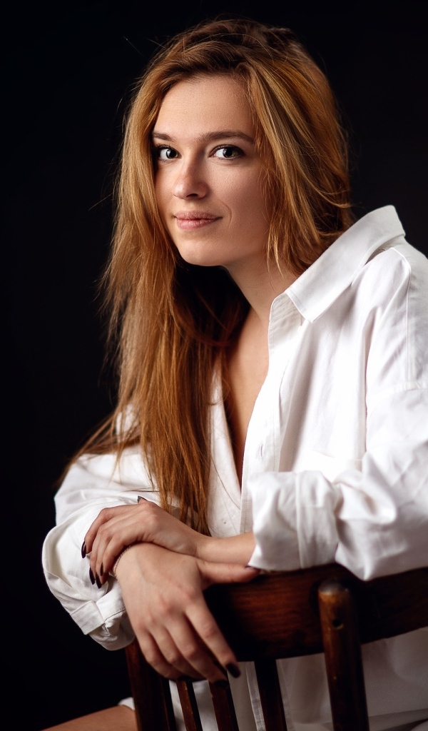 Милая девушка в белой рубашке сидит на стуле