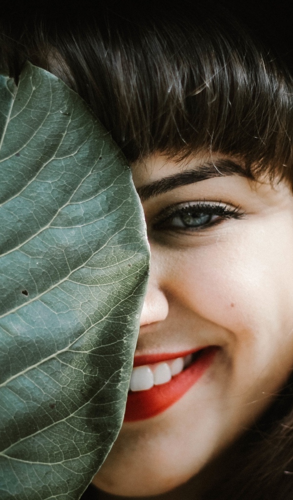 Милая улыбающаяся девушка прикрыла лицо листом