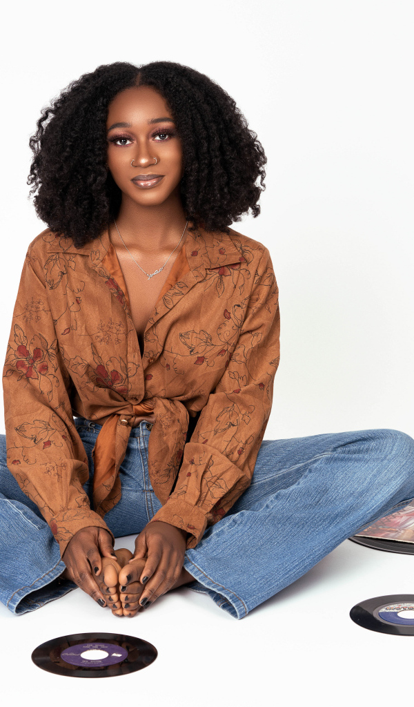 Темнокожая девушка сидит на белом фоне с пластинками