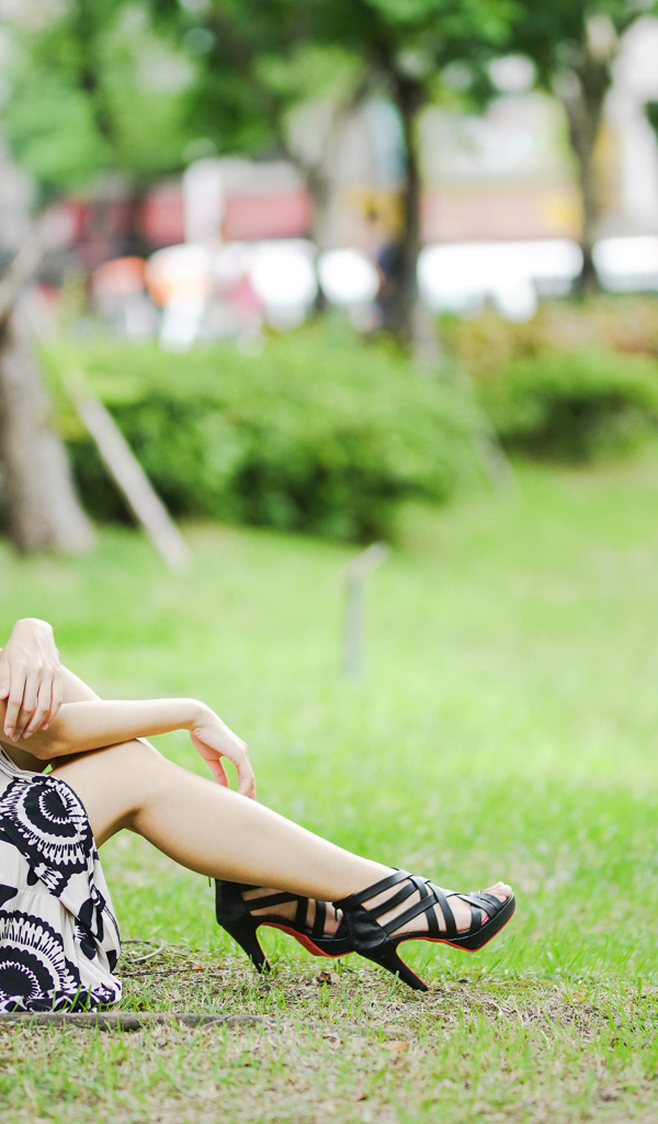 Мечтательная девушка азиатка сидит на траве в парке