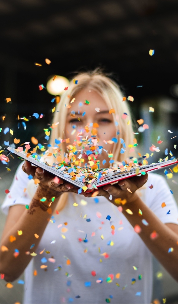 Девушка сдувает конфетти с книги 