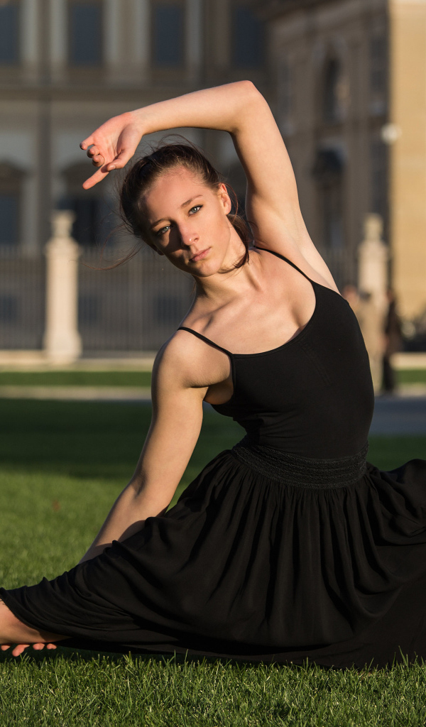 Девушка гимнастка в черном платье на зеленой траве