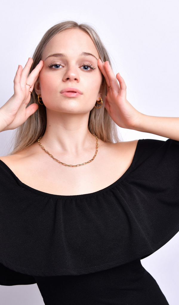 Девушка в черном платье с руками у головы на белом фоне