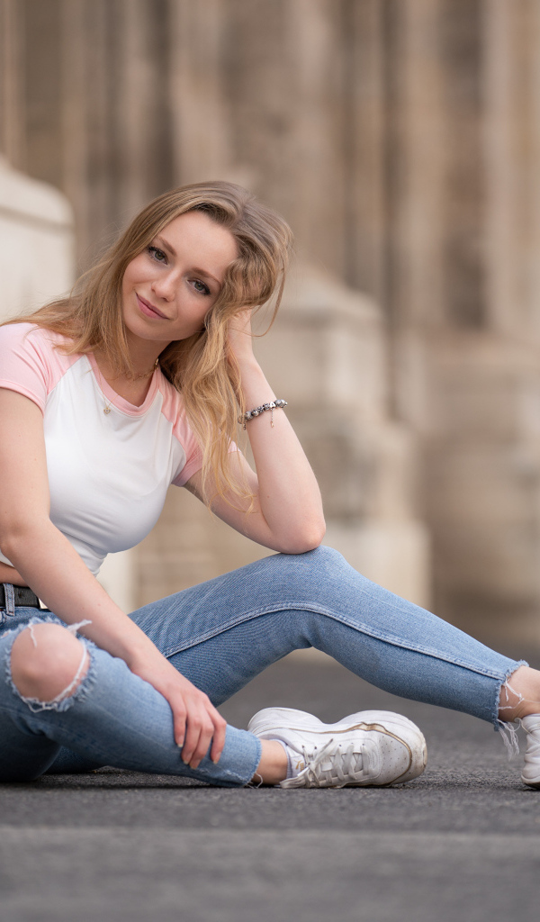 Девушка в рваных джинсах сидит на асфальте