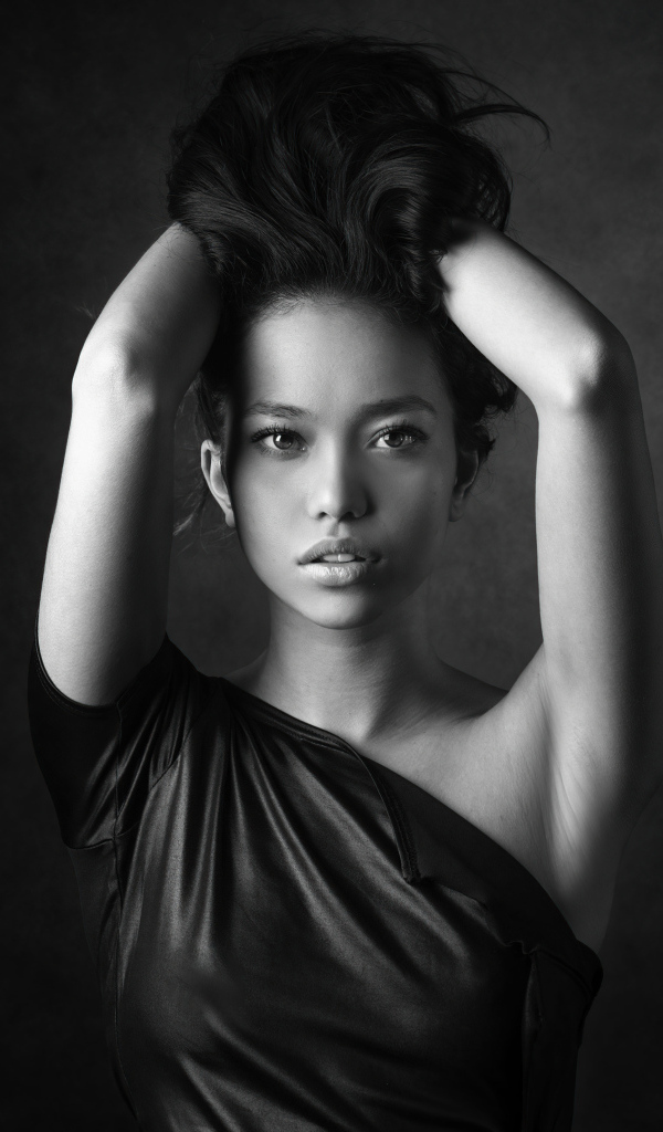 Девушка модель с руками в волосах  у стены