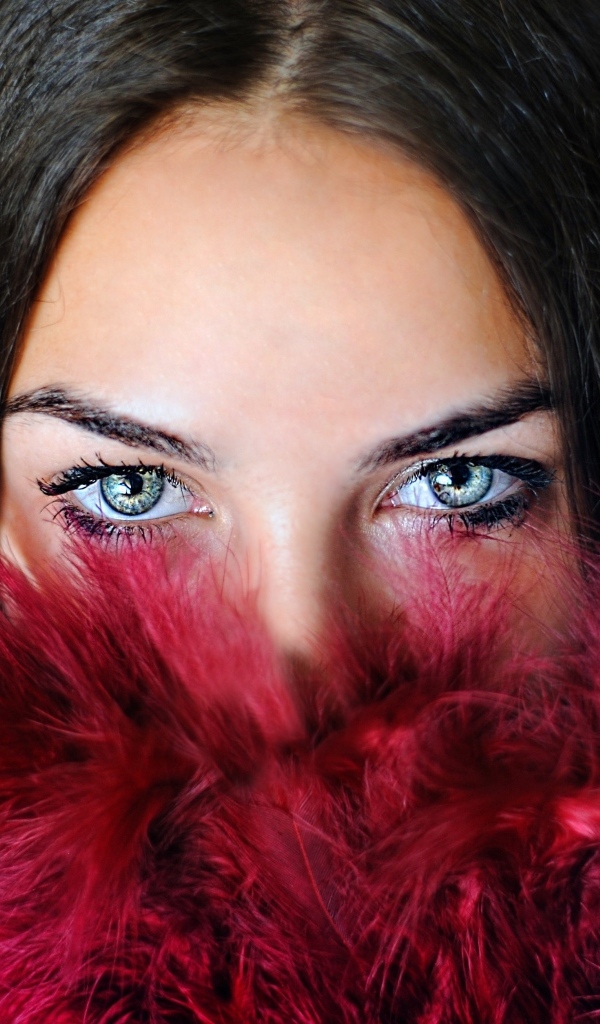 Девушка с красивыми глазами закрыла лицо красными перьями