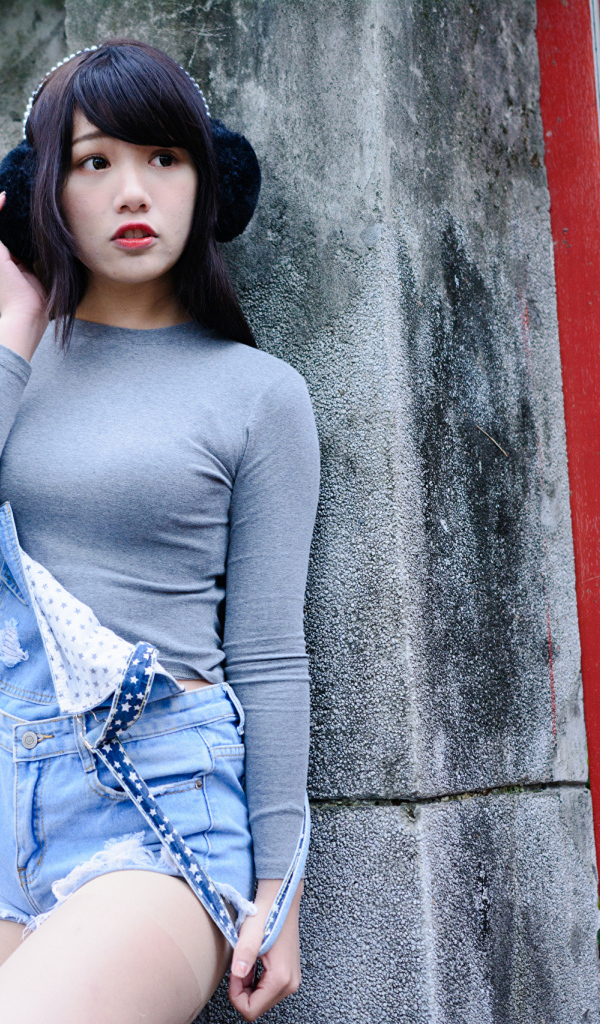 Скромная девушка азиатка в наушниках стоит у стены