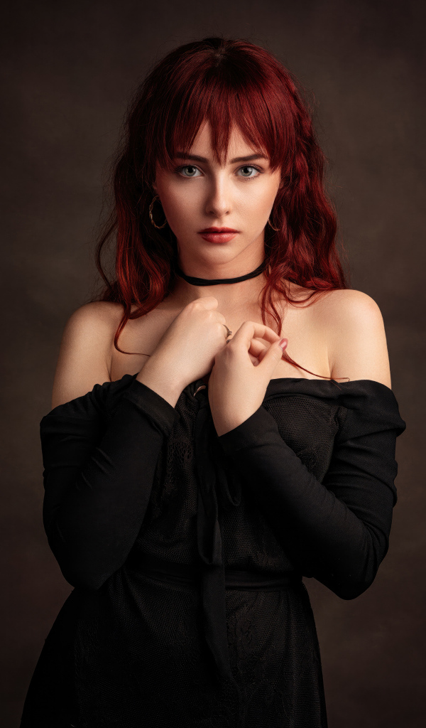Рыжеволосая девушка в черном платье у стены