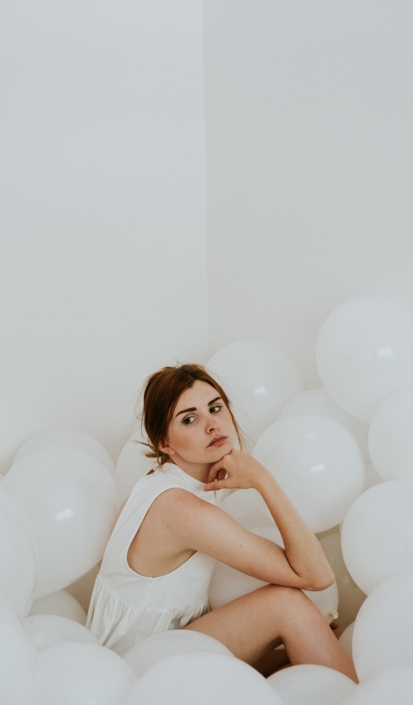 Грустная девушка сидит в белых воздушных шариках