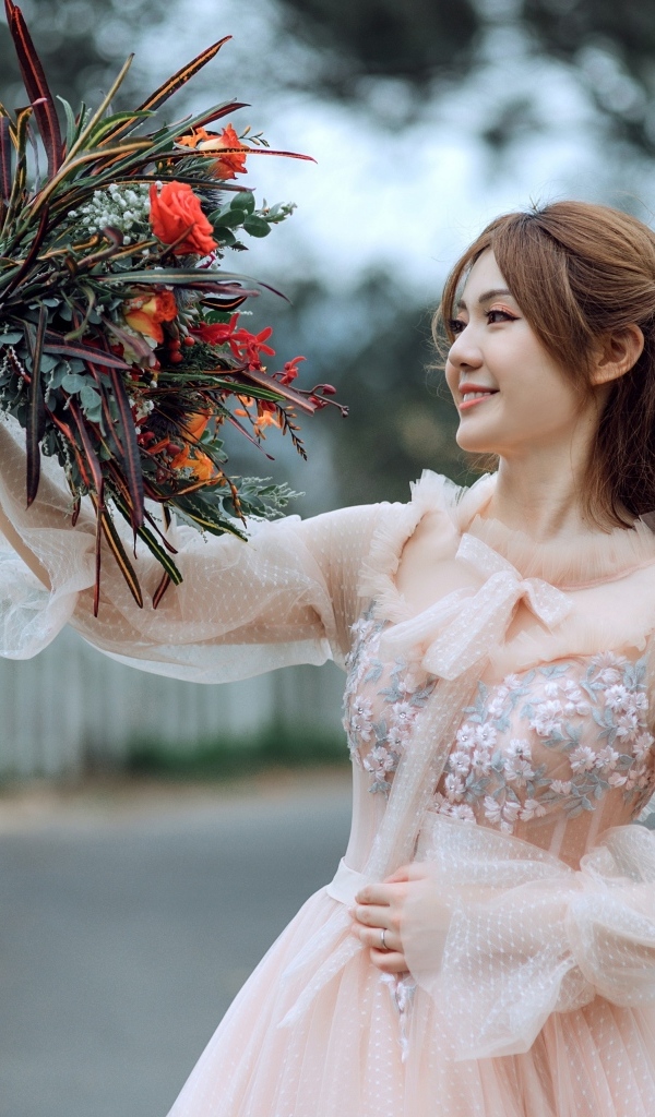 Улыбающаяся девушка азиатка в розовом платье с букетом