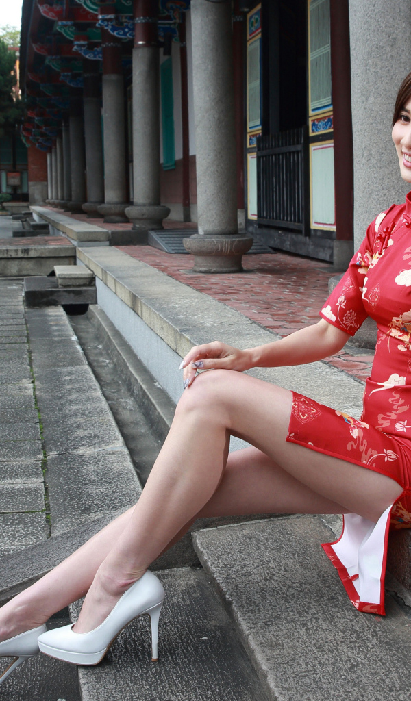 Улыбающаяся девушка азиатка в красном платье сидит на ступеньках