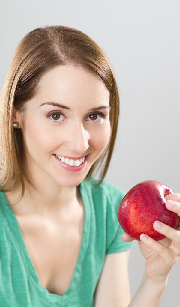 Улыбающаяся девушка с красным яблоком в руках