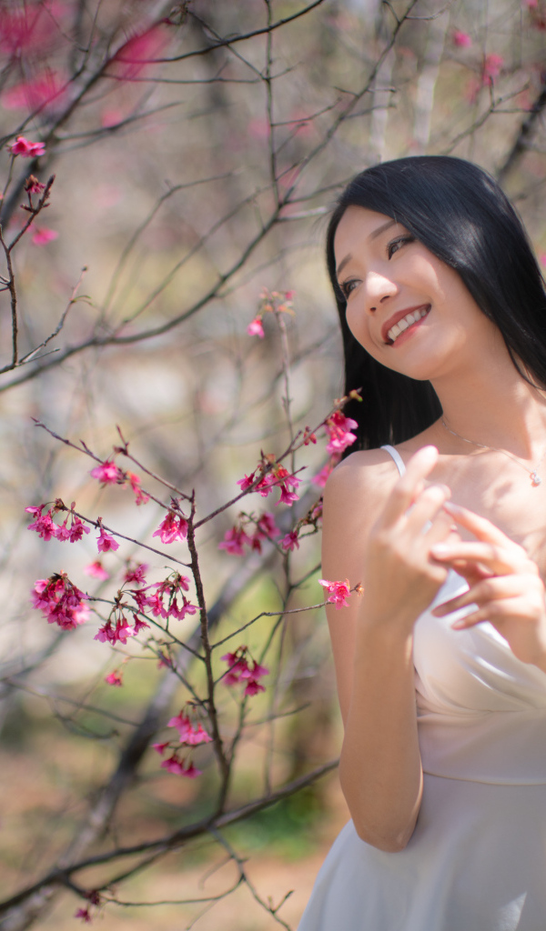 Улыбающаяся девушка в белом платье у дерева с цветами