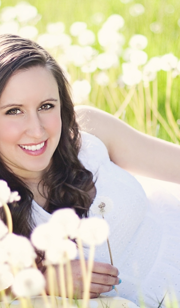 Улыбающаяся девушка лежит на поле с одуванчиками