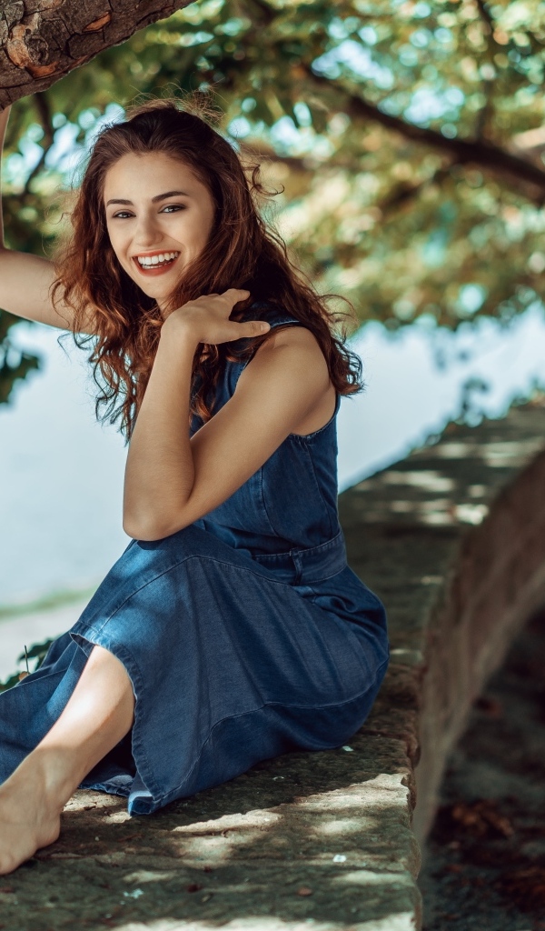 Улыбающаяся девушки сидит у дерева