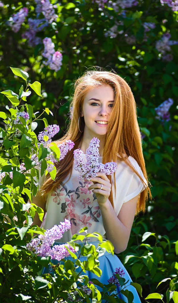 Улыбающаяся девушка стоит у куста сирени