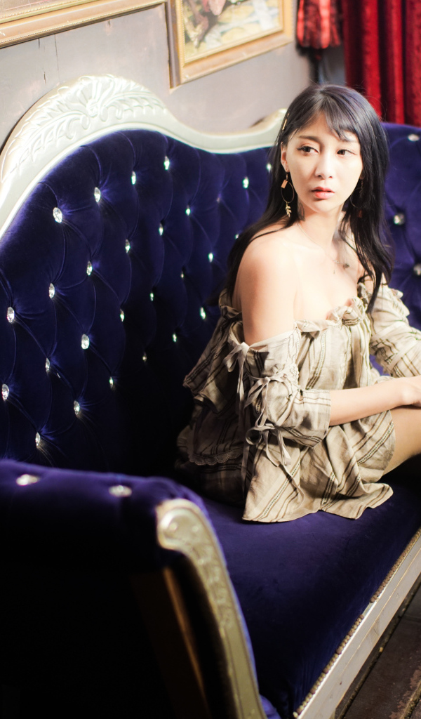 Молодая азиатка сидит на красивом диване