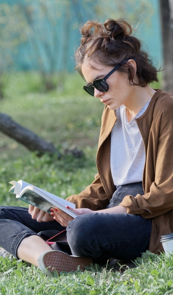 Молодая девушка сидит под деревом с книгой