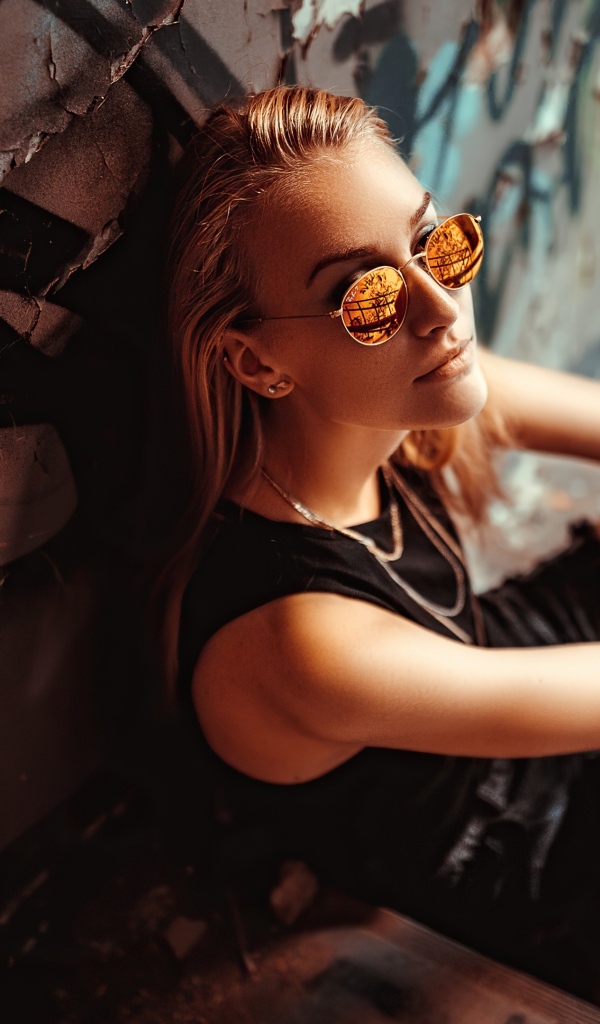 Молодая девушка в очках сидит у стены